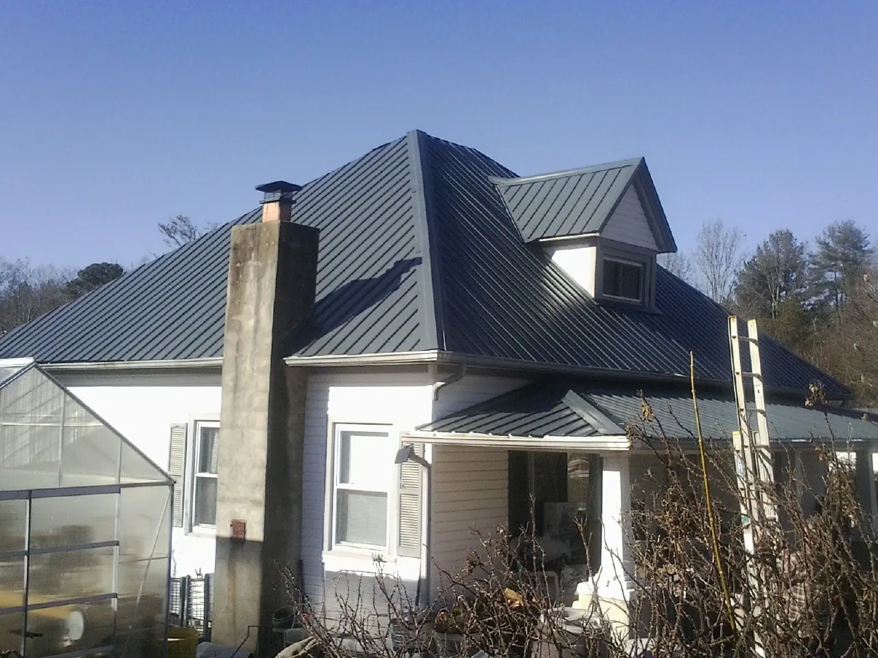 Dark blue standing seam metal roof on a white farmhouse with dormer — Slate & Tile Roof Repair by Roofing Brothers in Oak Hill
